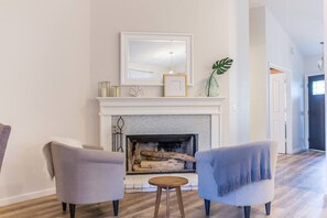 A living room with a fireplace, two armchairs, a small table, and a plant.