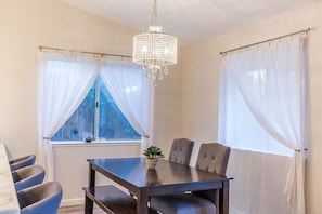 A dining area with a table, chairs, a chandelier, and sheer curtains.