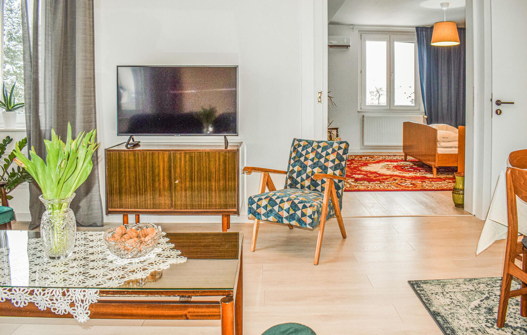 A living room with a TV, wooden furniture, a patterned armchair, and a red carpet.