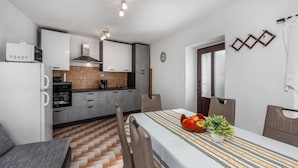 A compact kitchen with white cabinets, a microwave, and a coffee maker. There is a dining table with a patterned tablecloth and a vase of flowers. - Awesome home in Grizane (Grizane)