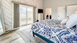 Ein Schlafzimmer mit einem großen Bett, einem Deckenventilator, einem Fernseher und Blick ins Freie.