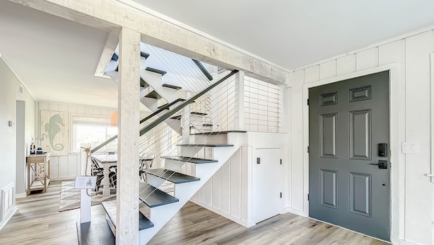 Eine moderne Treppe mit weißen und schwarzen Akzenten, die zu einem Raum mit einer dunklen Tür und Holzboden führt.