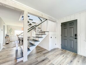 Een moderne trap met witte en zwarte accenten, die leidt naar een kamer met een donkere deur en houten vloer.