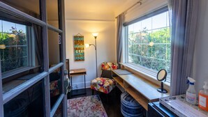 Een knus kamertje met een groot raam, een bureau, een stoel, een tafeltje en een spiegel.