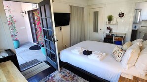 Een hotelkamer met een bed, een bureau, een stoel, een plafondventilator, een televisie en een kleine kitchenette.
