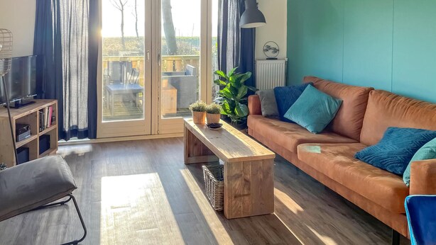 A living room with a sofa, a coffee table, a TV, and a balcony with curtains.