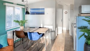 A modern kitchen with a wooden table, two chairs, a refrigerator, and a clock on the wall.