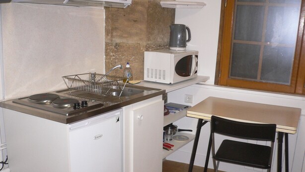 Une petite cuisine équipée comprenant une cuisinière, un évier, un four à micro-ondes et une petite table avec une chaise.