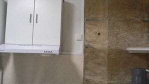Une cuisine avec un réfrigérateur blanc, un mur en pierre et une petite étagère.