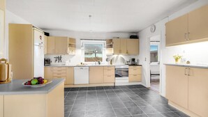 Une cuisine moderne avec des meubles aux finitions en bois clair, un îlot central et un sol carrelé de couleur noire.