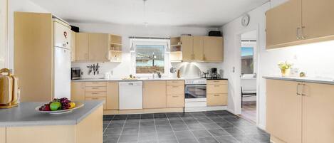 A modern kitchen with light wood cabinets, a central island, and a black tiled floor.