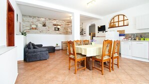 A dining area with a table and chairs, a sofa, a stone wall, and a kitchen area with cabinets and a TV.