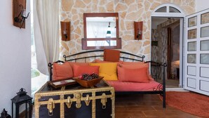 Een gezellige kamer met een stenen muur, een bed met oranje beddengoed, een houten kist en een raam met gordijnen.
