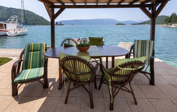 A covered outdoor seating area with a table and chairs, overlooking a body of water with boats and distant hills. - Gorgeous apartment in Blace with house sea view (Blace)