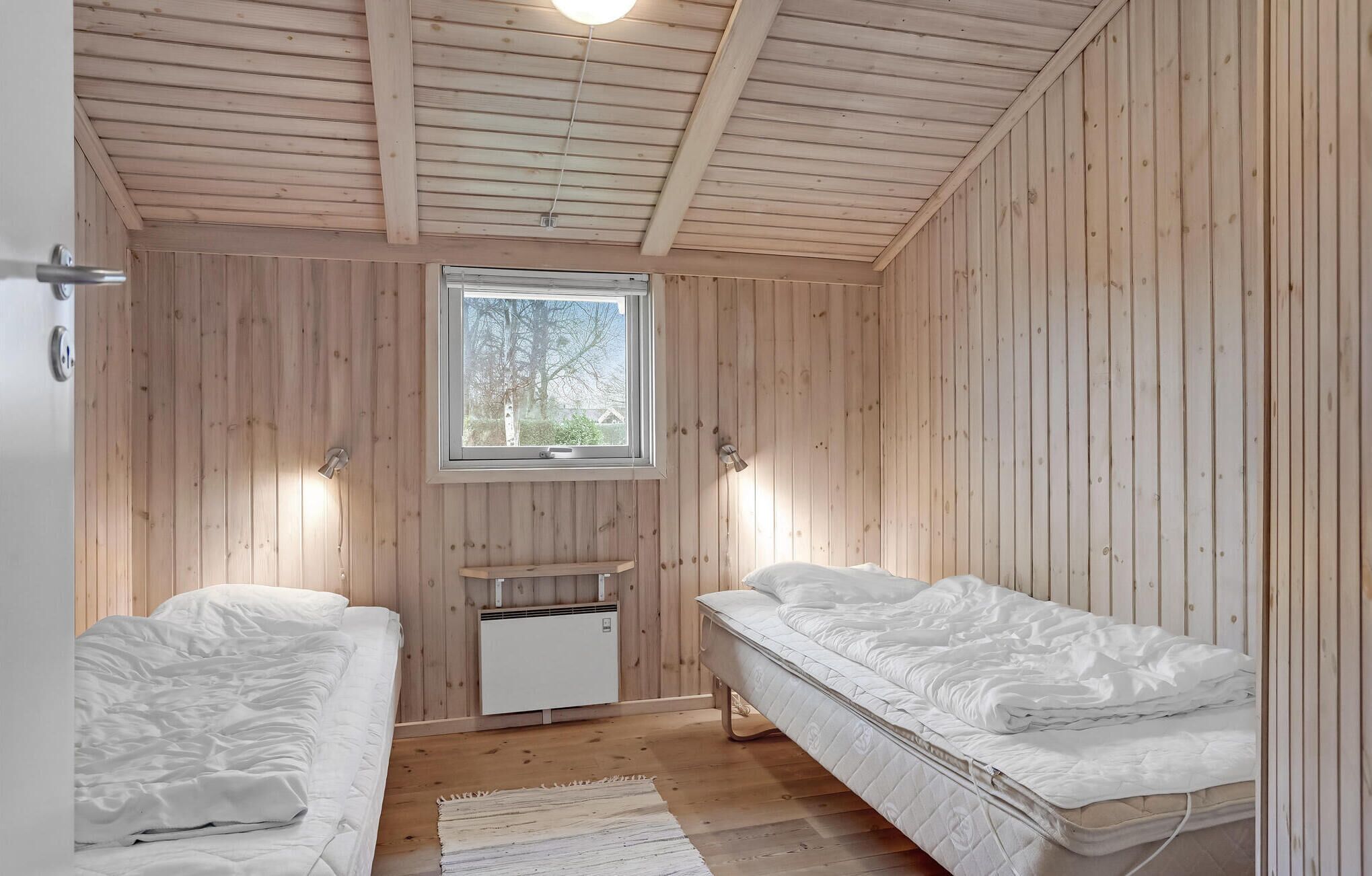 Una stanza con rivestimento in legno, due letti, una finestra e un piccolo termosifone.