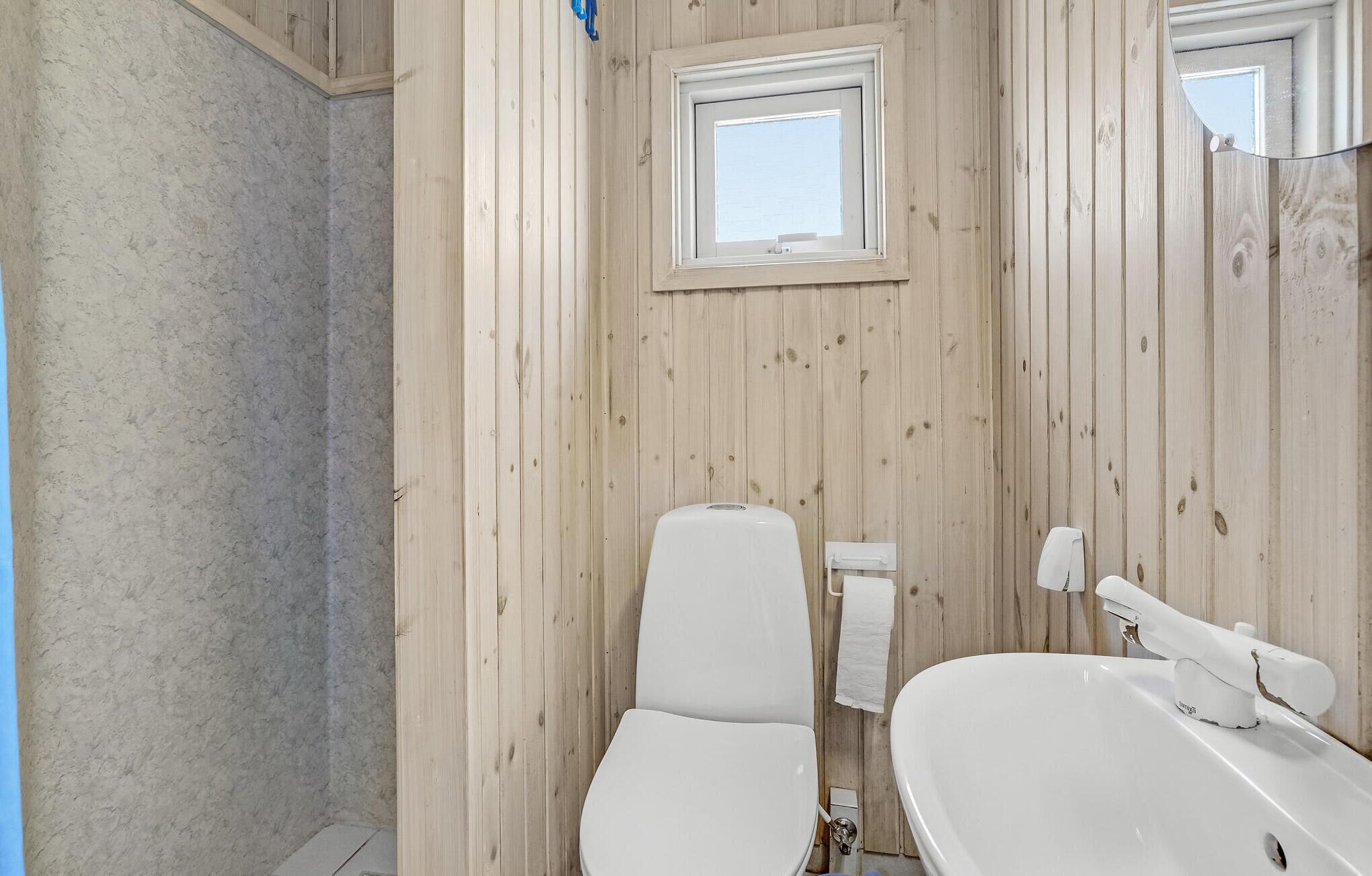 Une salle de bain avec des murs en bois, une fenêtre, des toilettes et un lavabo.