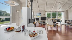 A spacious living room with a large window, a fireplace, and a dining area with a table set for breakfast. - Stunning home in Sydals with sauna (Sydals)