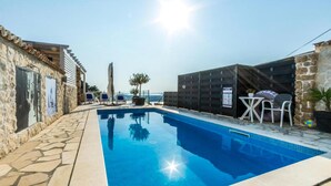 En swimmingpool med stenvægge, liggestole og et bord med stole.