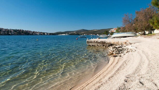 Una platja d'aigua cristal·lina, amb vaixells i un tram de roca.