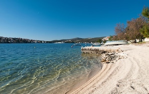 Ein Strand mit klarem Wasser, Booten und einer felsigen Küste.