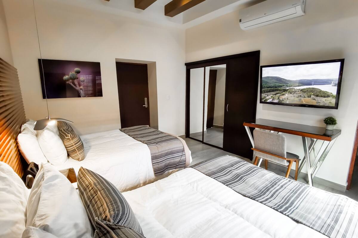 Une chambre d’hôtel moderne équipée de deux lits, d’un bureau, d’une télévision et d’une armoire à portes coulissantes.