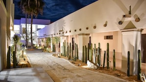 A desert-themed hotel corridor with a sandy pathway, cacti, and palm trees.