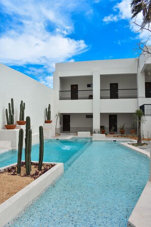 A pool area with a clear blue sky, white building with balconies, and cacti in pots. - Hotel Plaza Cuatrociénegas (Cuatro Ciénegas)