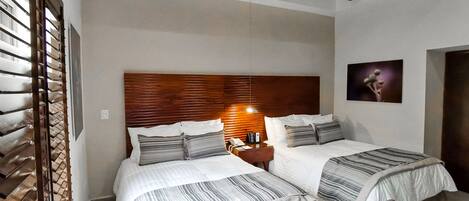 Habitación de hotel con dos camas, cabecero de madera, mesita de noche con lámpara y un cuadro en la pared.