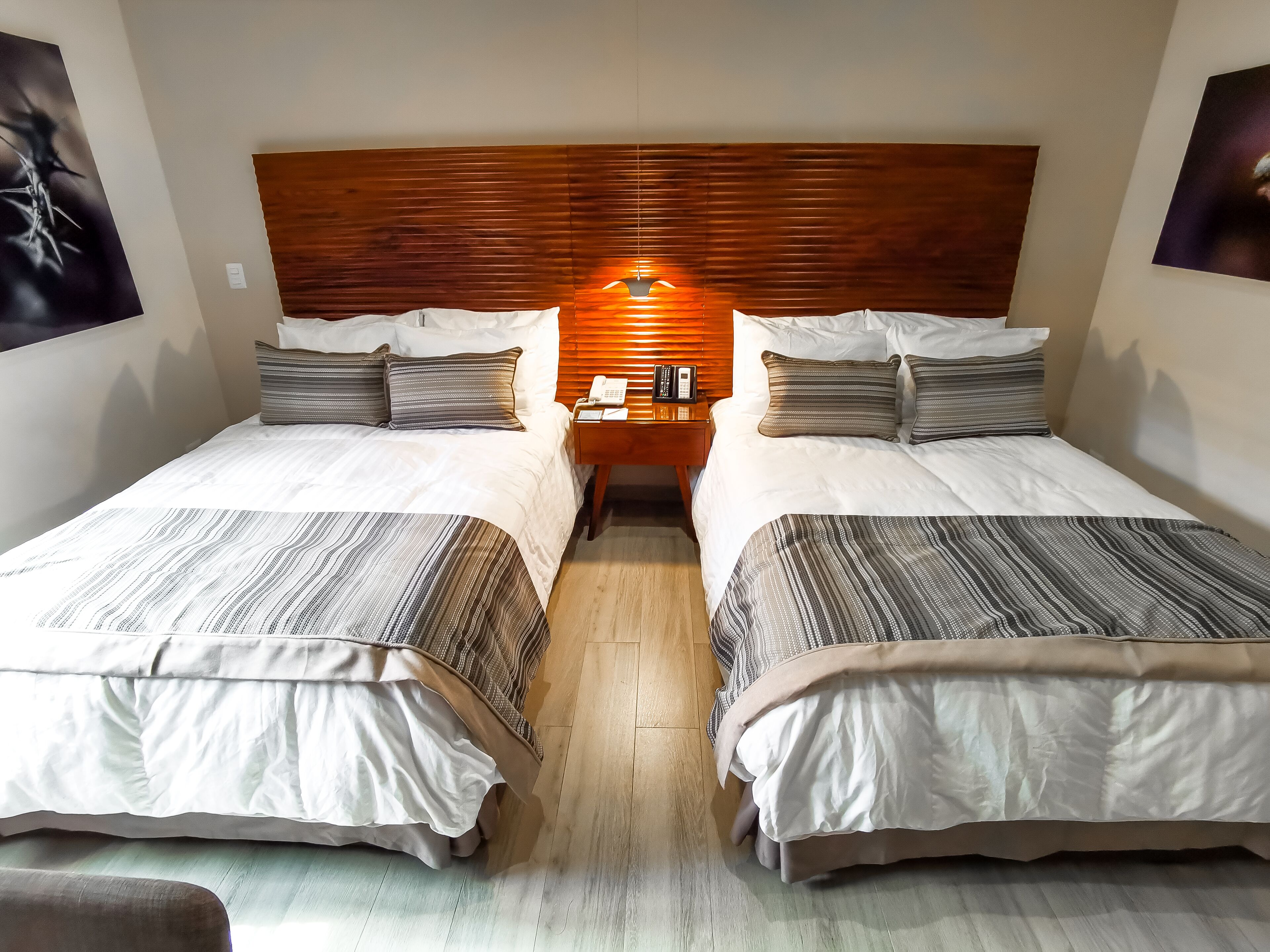 Une chambre d’hôtel avec deux lits, une tête de lit en bois, des tables de chevet avec des lampes et un plancher en bois.