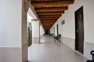 Un pasillo con suelo de baldosas, vigas de madera en el techo y un banco.