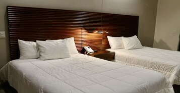 A hotel room with two beds, wooden headboard, white bedding, bedside tables, and a telephone.