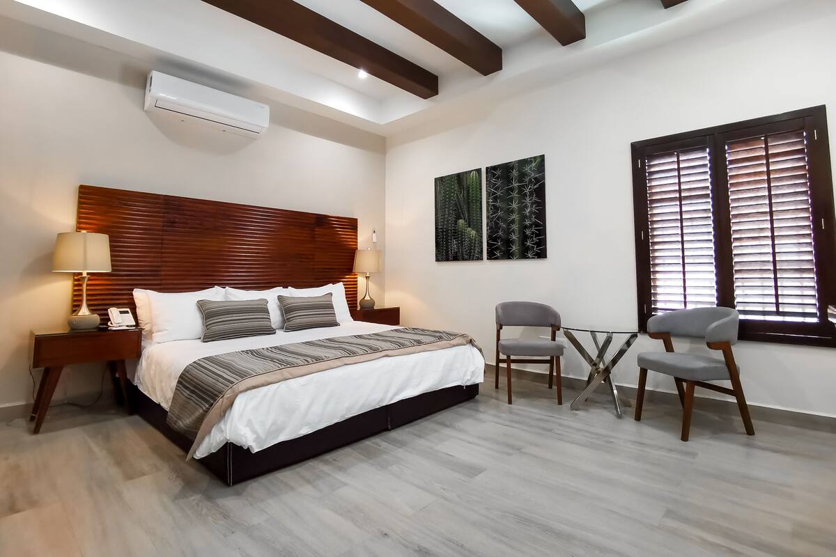 Une chambre d’hôtel comprenant un lit, deux chaises, une petite table, une table de chevet avec une lampe et des œuvres d’art accrochées au mur.