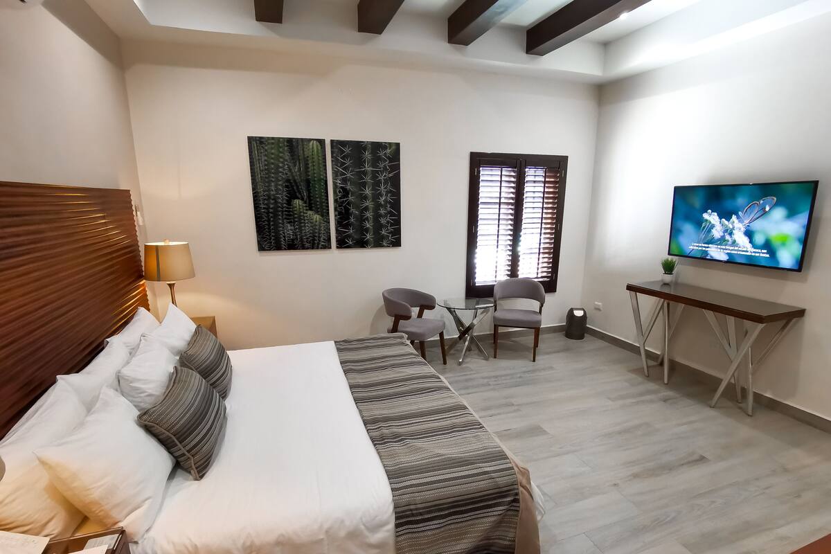 Une chambre d’hôtel moderne dotée d’un grand lit, d’un bureau, d’une télévision et de deux fenêtres équipées de stores.