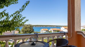 Un balcon avec une table ronde et des chaises, offrant une vue sur la côte, avec des maisons et un ciel dégagé.