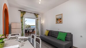 Un coin repas avec une table dressée pour deux personnes, un canapé gris avec des coussins verts et un tableau accroché au mur.