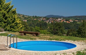A swimming pool with a wooden deck and metal ladders, surrounded by pebbles. In the background, there is a village with houses and a church on a hill. - Stunning home in Vrbovsko (Vrbovsko)