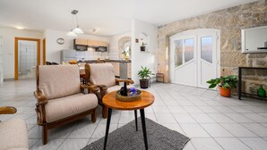 A spacious living area with a kitchen, two wooden armchairs, a round coffee table, and a stone wall. - Awesome apartment in Podpican (Podpican)
