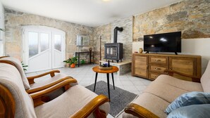 A cozy living room with stone walls, a fireplace, a television, and wooden furniture. - Awesome apartment in Podpican (Podpican)