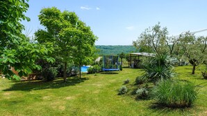 A grassy outdoor area with a trampoline, trees, and a view of a hilly landscape in the background. - Awesome apartment in Podpican (Podpican)