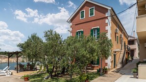 Un edificio a due piani con facciata rossa e persiane verdi, un patio con mobili da esterno e vista sul mare.