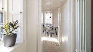 A hallway leading to a dining area with a table set for four, a potted plant on the windowsill, and a radiator on the wall. - Observatory House & Apartment (Edinburgh)
