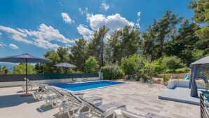 A swimming pool with lounge chairs and umbrellas, surrounded by trees and a stone wall. - Luxurious home in Imotski (Imotski)