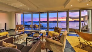 A spacious living room with a large glass wall offering a scenic view of a sunset over water. - Amazing home in Orasac (Orasac)