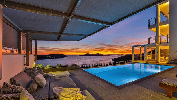 A rooftop pool area with a view of the sunset over the sea, a seating area with cushions, and a modern architectural design. - Amazing home in Orasac (Orasac)