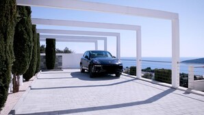 A modern car parked in a white-brick driveway with a clear view of the sea and hills in the background. - Amazing home in Orasac (Orasac)
