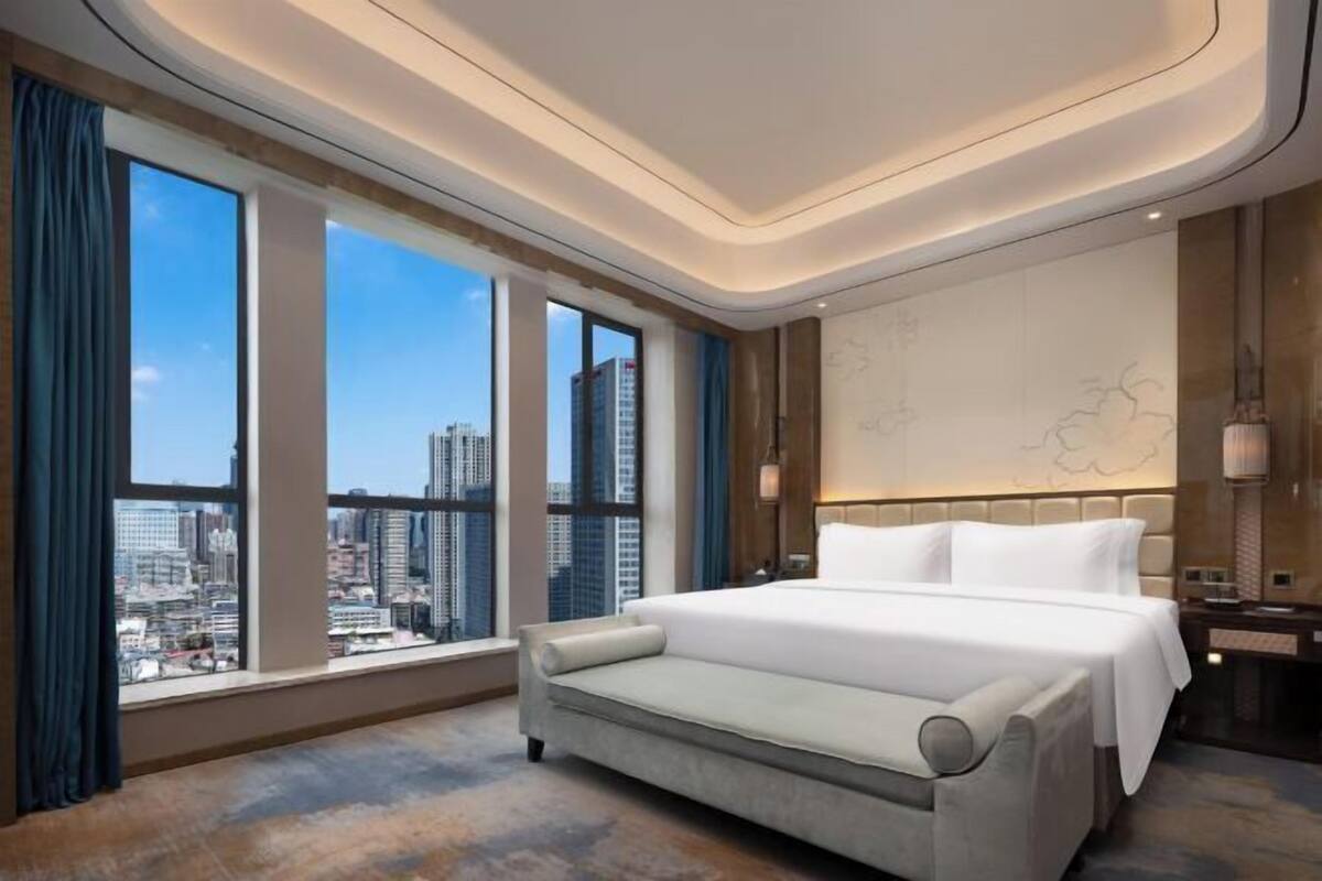 Ett modernt hotellrum med en stor säng, en soffa, utsikt över staden och en dekorativ vägg.