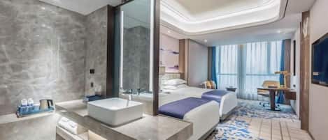 A modern hotel room with a large bed, a separate bathroom with a large mirror, and a small desk area.