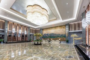 A spacious lobby with a polished marble floor, a large chandelier, and a reception desk.