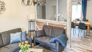 Un salon avec un canapé, une table basse ornée d’un vase de fleurs, une lampe et un mur en briques.