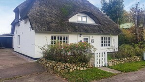 Une petite maison blanche au toit de chaume, dotée d’un petit porche et d’un mur en pierre.